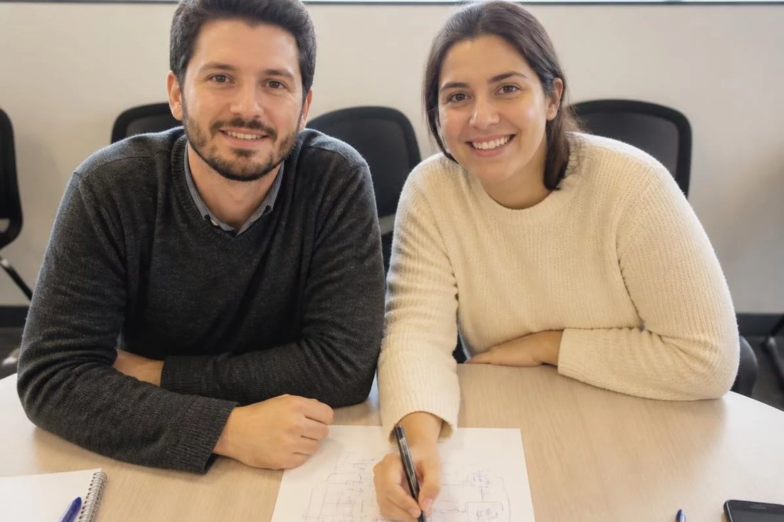 Dupla debruçada sobre um tablet apoiado na mesa de madeira, revendo as anotações da rodada anterior
